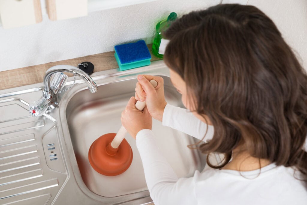 Woman Using Plunger In Sink.