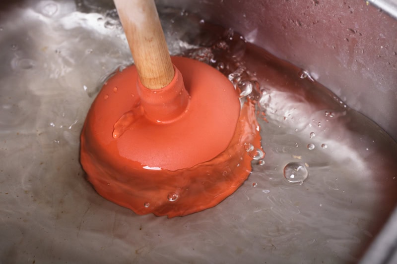 An Orange Cup Plunger In sink Filled With Water.