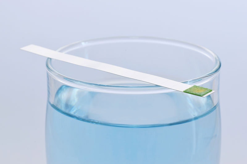 A water testing strip on top of a glass.