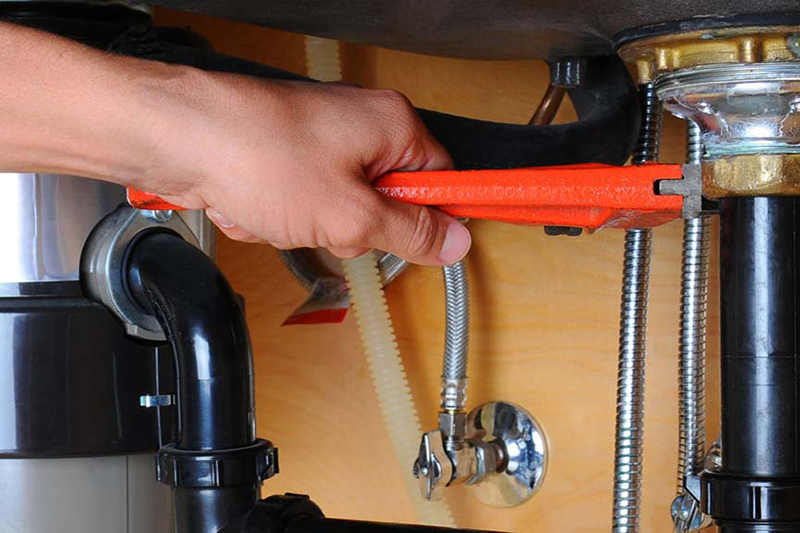2025 Guide to Garbage Disposals. Photo of a hand performing maintenance on a garbage disposal underneath a sink.