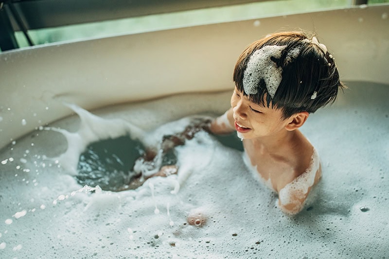 Tank vs. Tankless: Which Water Heater is Right for Your Valparaiso Home? Photo of a young boy playing in the bathtub.