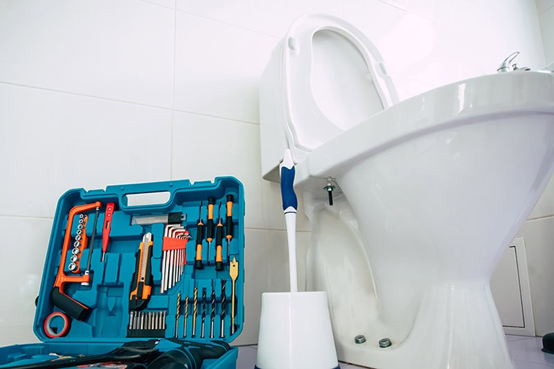 How to Unclog Your Slow-Draining Toilet in Crown Point. Close up photo of ceramic bowl toilet in domestic bathroom with a box of tools.